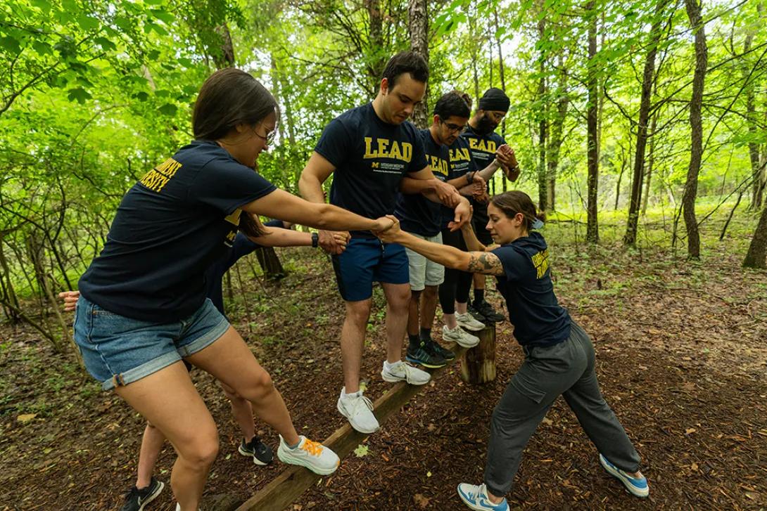 Students on a balance beam in the woods working together