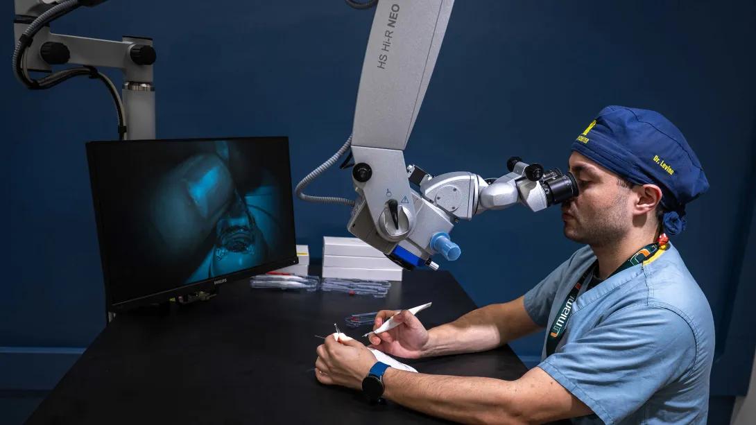 Resident practices delicate ophthalmic surgery techniques using a microscope.