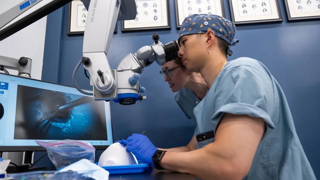 Ophthalmology residents collaborate at a surgical microscope during wet lab training.