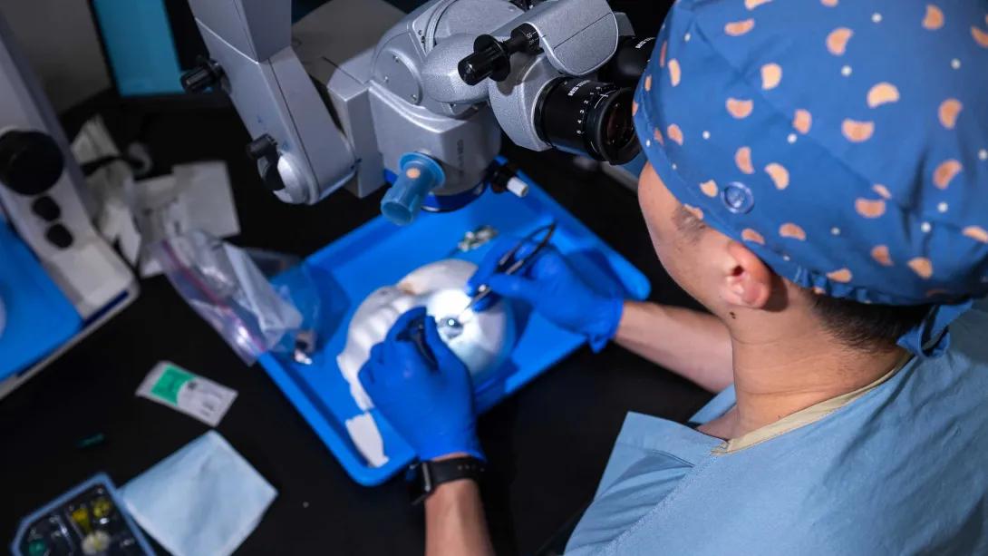 Resident practices eye surgery on a training model under a surgical microscope.