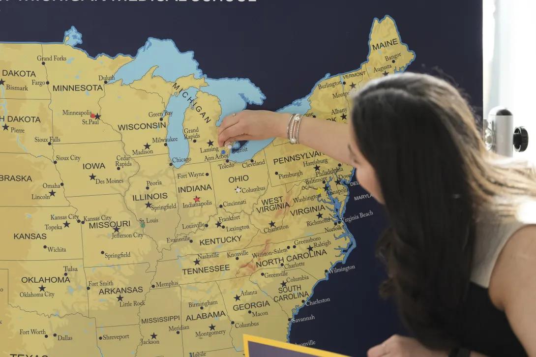A person reaches toward a large U.S. map display, placing a marker near Michigan and the Great Lakes.