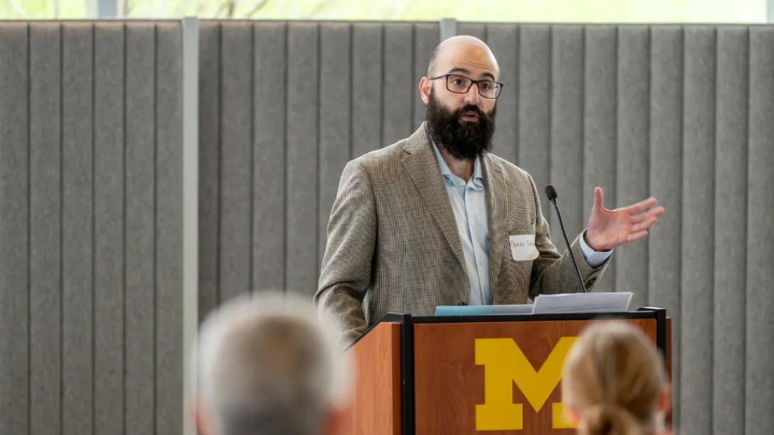 A presenter gestures while speaking at a University of Michigan podium during the Department of Anesthesiology Research Retreat.