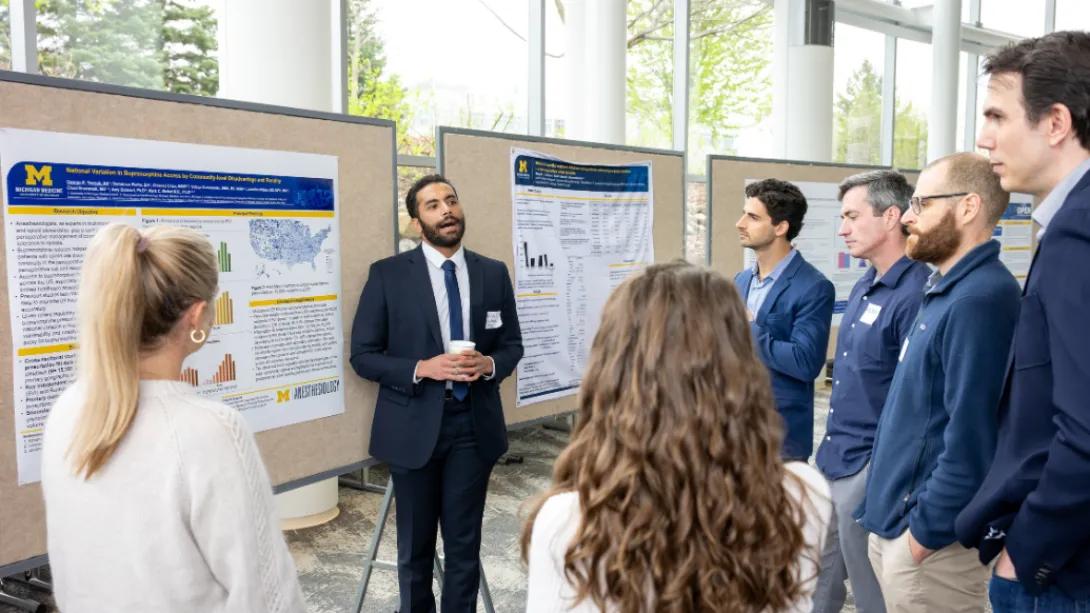 A student researcher presents a poster to a group of attendees during the Department of Anesthesiology Research Retreat poster session.