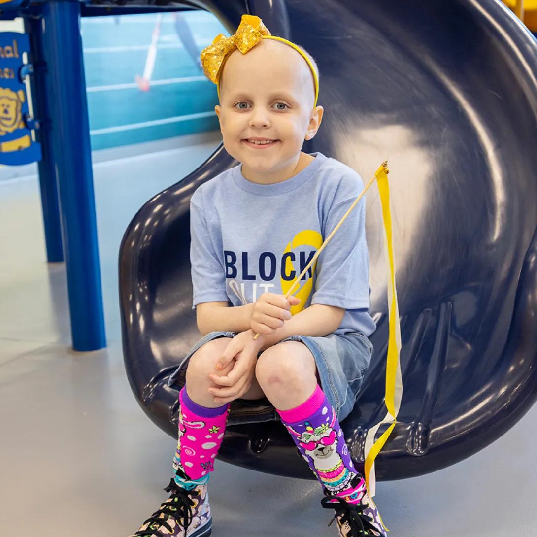 A child wearing a Block Out Cancer t-shirt and colorful socks sits at the bottom of a slide.