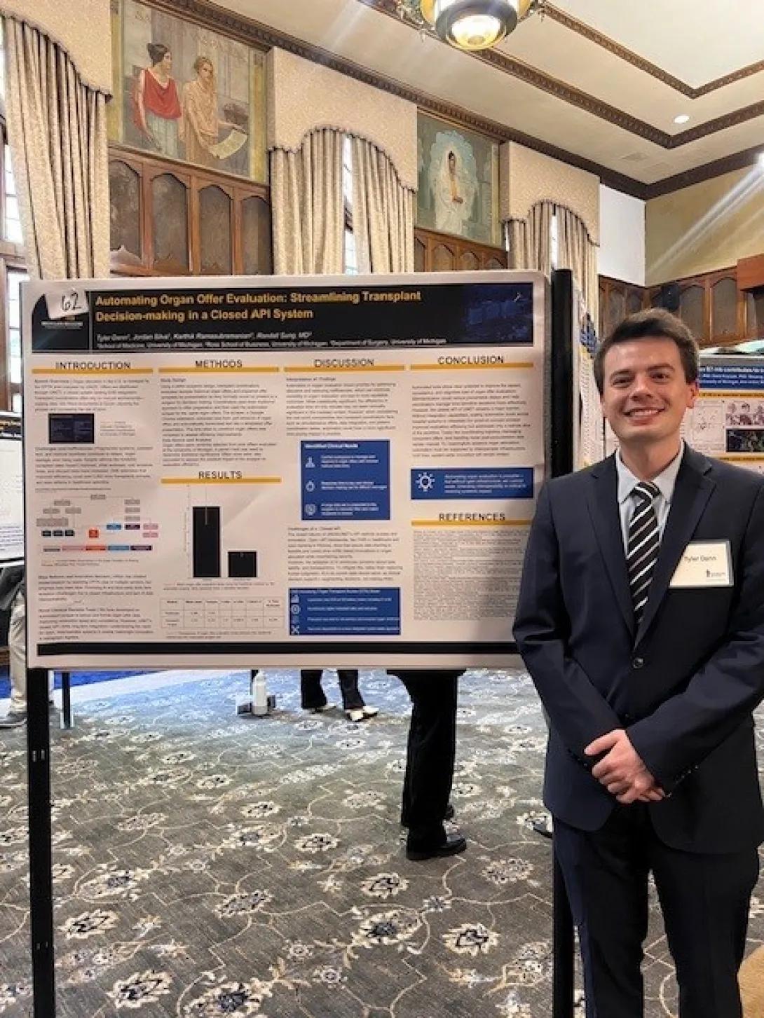 A person in a suit stands smiling beside a research poster titled “Automating Organ Offer Evaluation: Streamlining Transplant Decision-making in a Closed API System” at an indoor academic poster session.