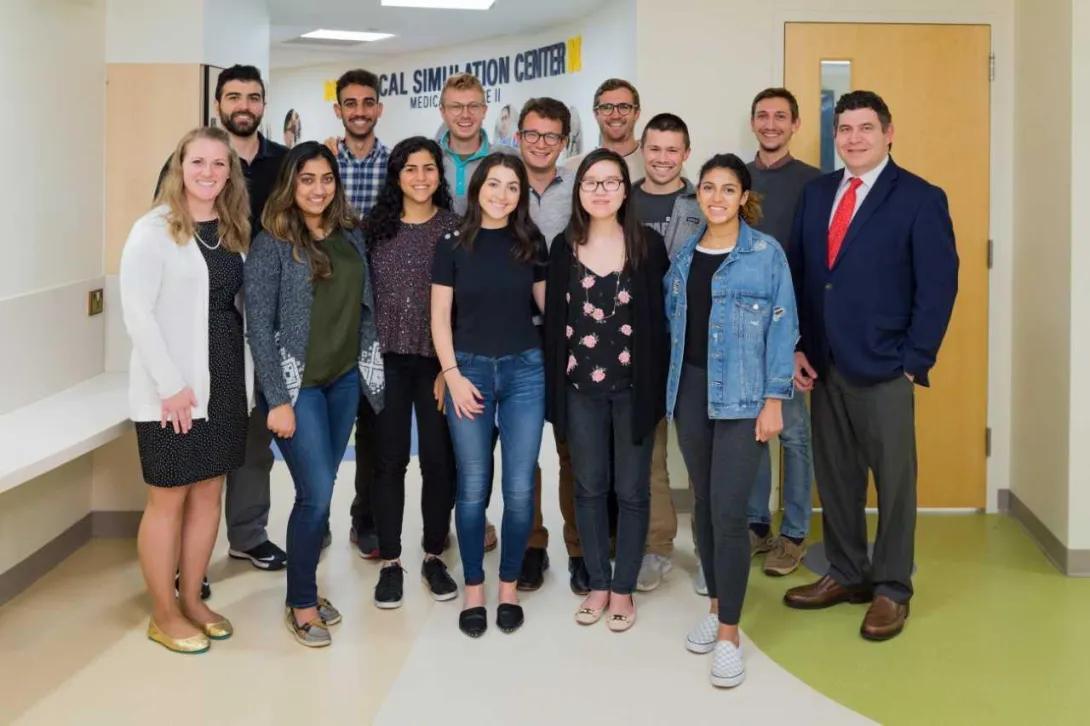 Fourteen people pose together in a hallway outside the University of Michigan Medical School's Clincial Simulation Center.